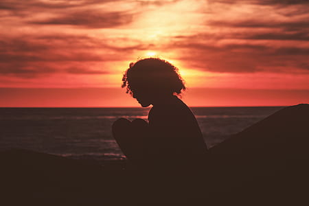 silhouette of woman sitting near body of water during sunset thumbnail