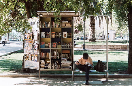 man in orange shirt sitting on bench beside bookshelf thumbnail
