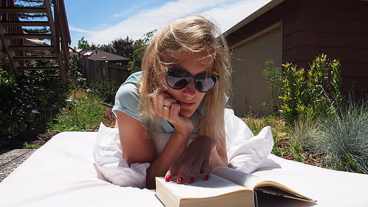 woman wearing black sunglasses reading book under cloudy blue sky during daytime thumbnail