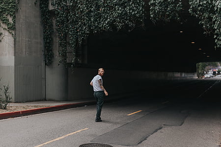man in shirt stands near road tunnel with green vines at daytime thumbnail