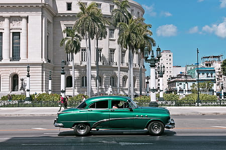 green sedan crossing road near white concrete building at daytime thumbnail