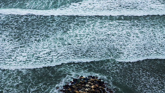 bird's eye photography of rocks on shore with ocean waves thumbnail