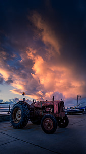 red farming tractor under cumulus clouds thumbnail