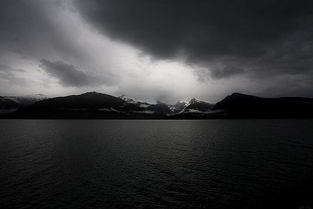 ocean near mountain under gray sky thumbnail