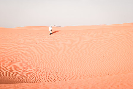 person walking in the desert terrain during daytime thumbnail