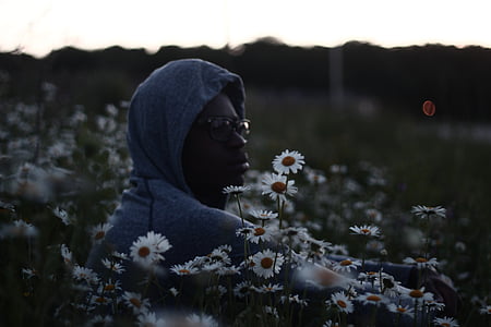 man in grey hoodie sitting on white chamomile field thumbnail