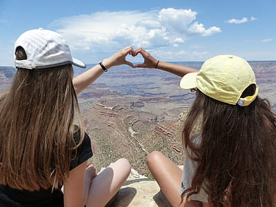 two women sitting on gray surface while making heart gesture with both of their hands thumbnail