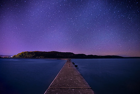 brown wooden dock between body of water during nighttime thumbnail