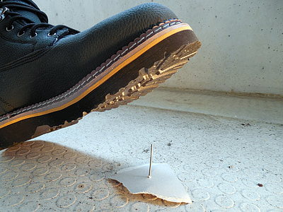 close-up photo of person wearing black leather work boot about to step on gray metal needle thumbnail