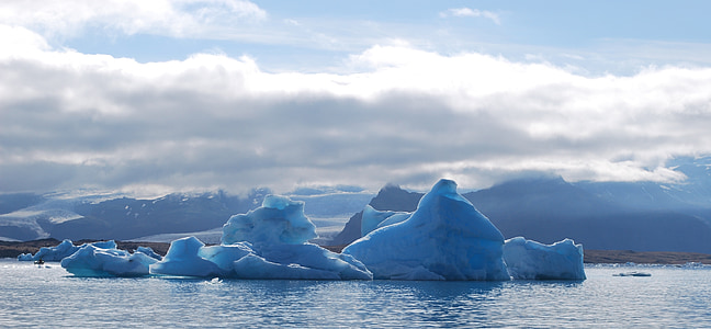 ice bergs floating on sea under cloudy blue sky thumbnail