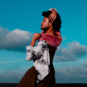 man wearing brown and white floral dress standing thumbnail