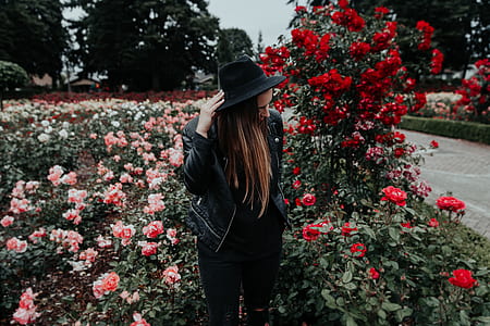 woman in black jacket standing near red and pink flower thumbnail