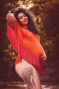woman wearing orange lace tops with red fringed holding her head and stomach on body of water thumbnail