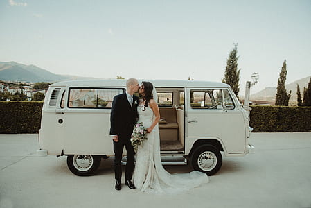 woman in white wedding dress kissing man in black suit outdoors thumbnail