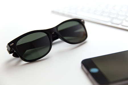 Sunglasses, mobile iPhone smartphone and computer keyboard on a white office desk thumbnail