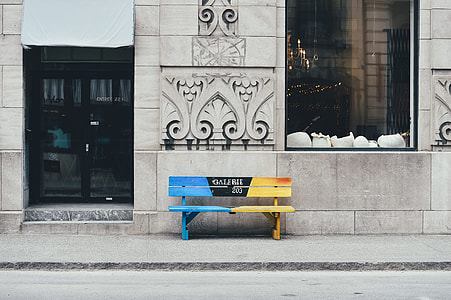 blue and yellow wooden bench beside gray concrete building thumbnail