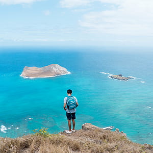 person standing in front of cliff far at brown rock formation under blue sky thumbnail