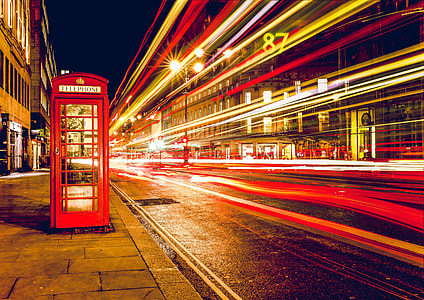 red telephone booth on concrete ground near buildings at nighttime thumbnail