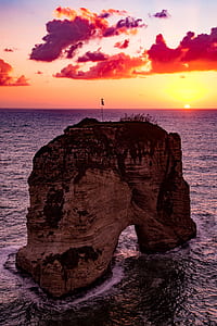 silhouette photo of brown cliff on water during golden hour thumbnail