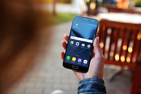 A young woman uses her smartphone Galaxy S7 outside on the pavement café thumbnail