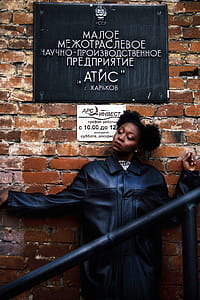Woman in Black Leather Coat Leaning on Brick Wall thumbnail