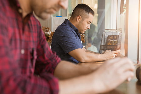 closeup photo of man wearing red and black 3/4-sleeved shirt sitting near man wearing blue polo shirt during daytime thumbnail