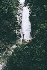 person standing on rock formation in front of waterfalls during daytime thumbnail