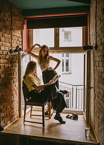 woman sitting reading book beside woman standing looking at book inside room thumbnail