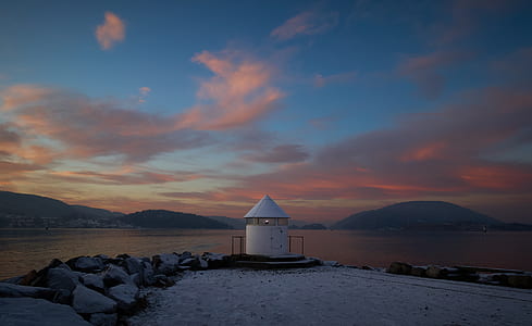 white and black concrete shed near body of water and mountain at golden hour thumbnail