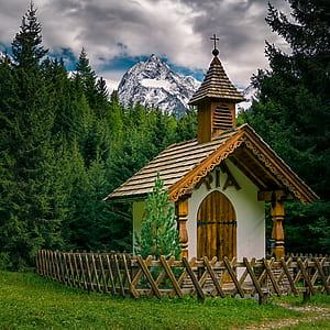 white and brown wooden chapel beside green pine trees across glacier mountain under white and blue cloudy skies thumbnail