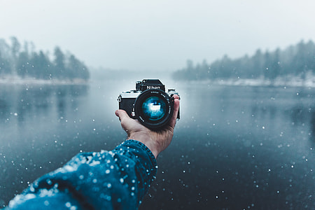 person holding camera taking photo in front of body of water thumbnail