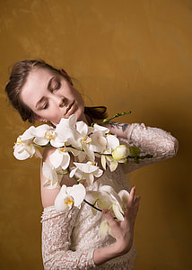 woman holding white moth orchids near brown wall thumbnail
