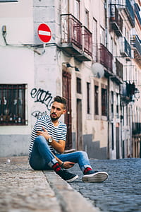 man sitting at the sidewalk near buildings during day thumbnail