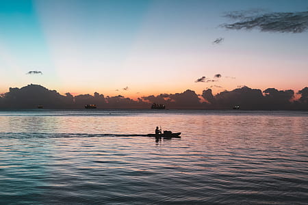 silhouette photography of person riding on canoe surrounded by body of water during golden hour thumbnail