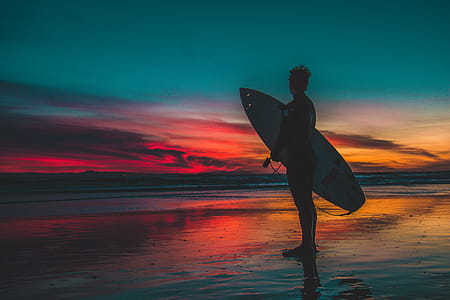 Silhouette of Man in Wet Suit Holding White Surfboard While Standing on Beach during Golden Hour thumbnail