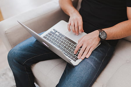 man wearing black shirt and blue denim jeans with MacBook Air on lap thumbnail