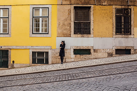 woman leaning on yellow and white building during daytime thumbnail