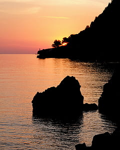 silhouette photo of rock on sea during golden hour thumbnail
