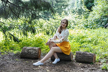 woman wearing white and multicolored long-sleeved shirt and yellow miniskirt outfit sitting on log at daytime thumbnail