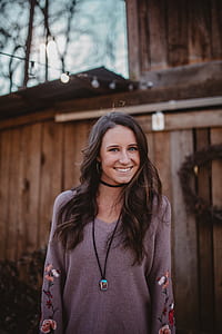 woman in gray top standing beside brown wooden house during daytime thumbnail