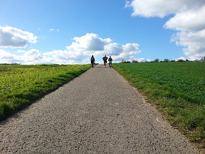 three person walking on pathway between grass during daytime thumbnail