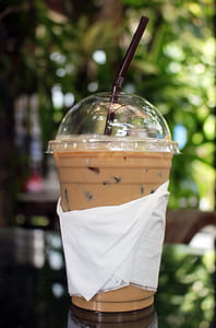 Cup of iced coffee outside on a table in a tropical garden thumbnail