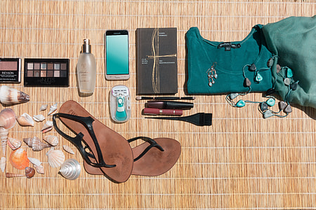 pair of black leather sling-back sandals; Android smartphone; makeup palette; seashells on brown wicker surface thumbnail