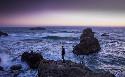 Man in Black Shirt Standing on Rock in Between Sea Water thumbnail
