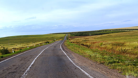 road between grass field under white clouds during daytime thumbnail