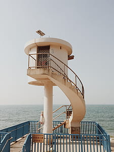 beige concrete tower near body of water under cloudy sky thumbnail