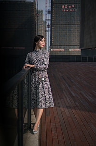 woman in white and black floral dress standing beside black railing while looking to her left side and smiling thumbnail
