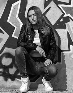 grayscale photography of woman wearing leather jacket and jeans with pair of sneakers thumbnail