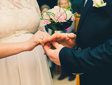 woman wearing white wedding dress and man wearing black suit holding a ring thumbnail