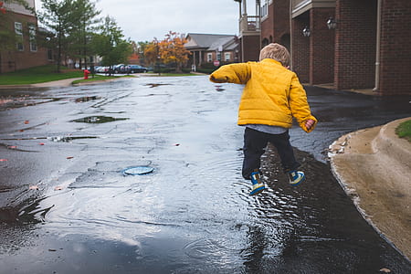 boy in yellow jacket jumping over wet road thumbnail